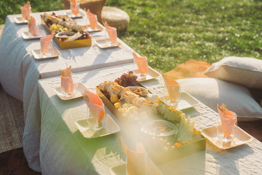 Picknicktische im Park mit Grazing Platten von Feasts of Eden, Palmblatttellern, Gläsern und rosafarbenen Servietten