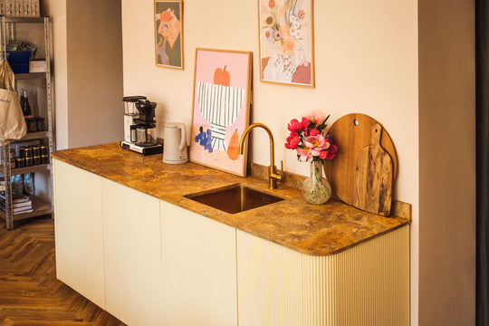 Beigefarbene Küchenanrichte mit Glasvase, Kaffeemaschine, hölzernen Schneidebrettern und modernen Bildern an der Wand