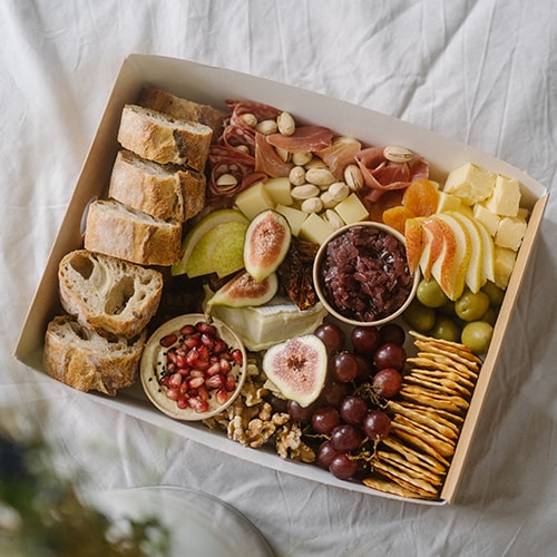Grazing Box mit Wurst, Käse, Chutney, Humus, Obst, Crackern und Baguette